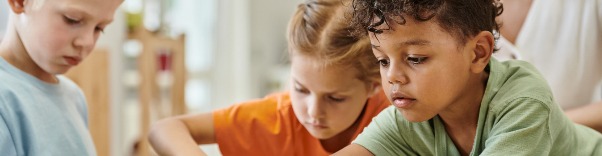 Three young children closely interact while focusing on an activity at a table, enjoying hands-on learning in a nurturing Pre-K School Care environment.