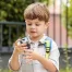 Little boy wearing a backpack, drinking water outside.
