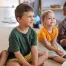 Group of small smiling children sitting on floor indoors in classroom.
